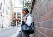 Young woman leaning on brick wall looking at mobile phone